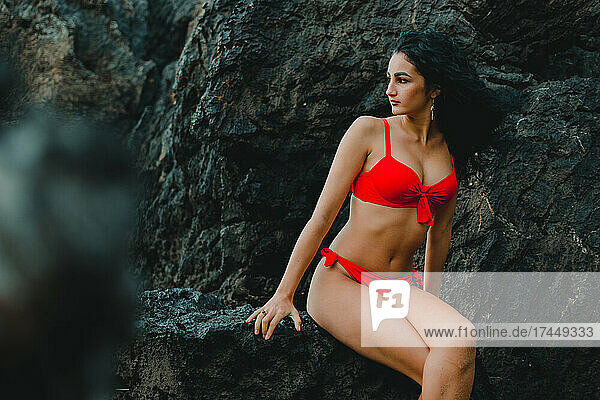 young woman posing in a red bikini on the rocks of a beach