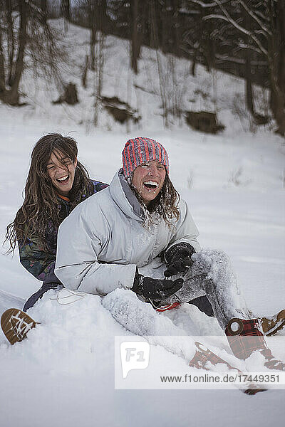 girlfriends laugh as they get covered in snow on toboggan