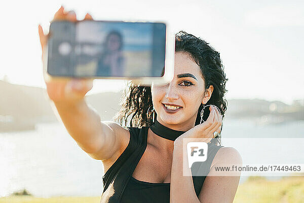 Happy young woman wearing black dress taking a smartphone in fro