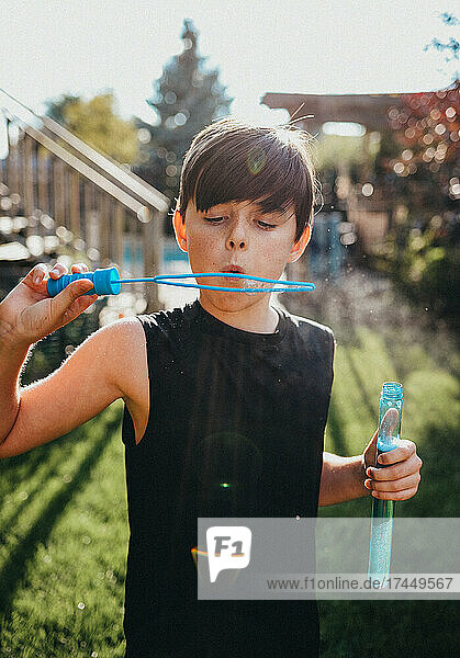 Young boy blowing bubbles in a backyard on a sunny day.