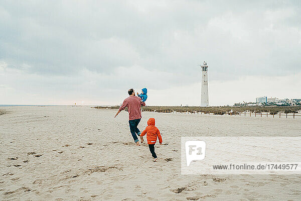 Father and children running in beach on cold cloudy day