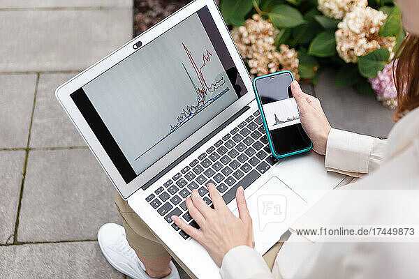 woman holding laptop and smartphone watching bitcoin growth chart