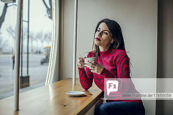 Brunette woman drinking coffee while looking out the window