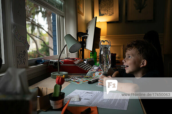 Boy excitedly creating a tornado in a bottle at his desk at home