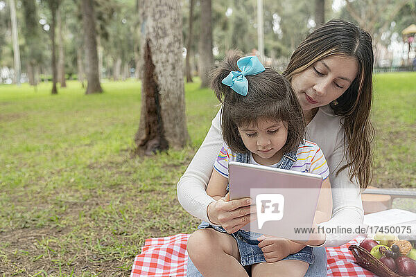 Mother and daughter using a tablet on a picnic tablecloth