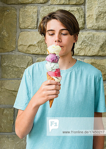 Teen boy eating large multiple scoop ice cream cone outside.