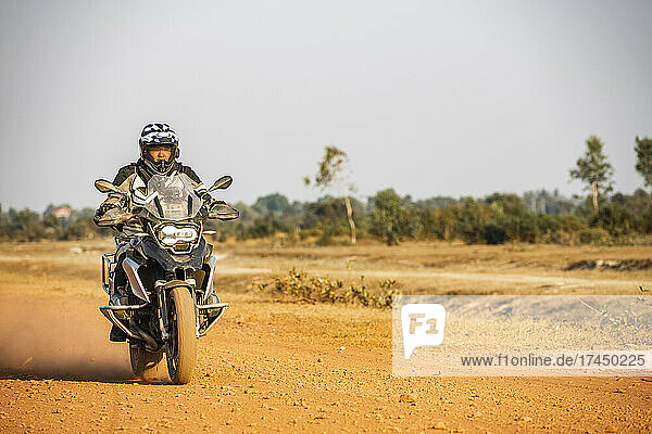 Man riding his adventure motorbike on dirt road in Cambodia