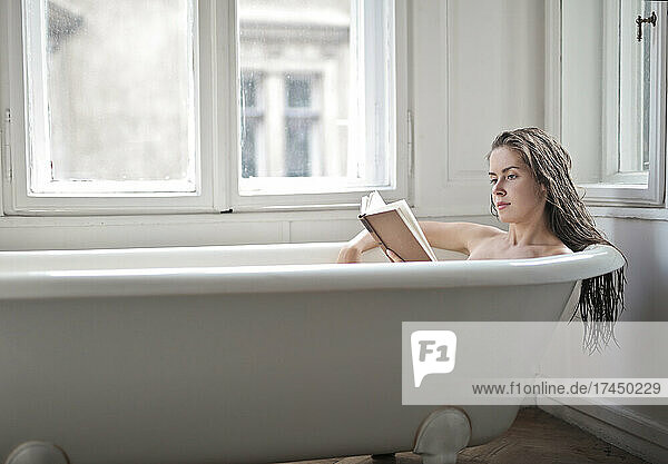 young woman in a bathtub reads a book
