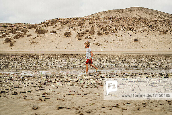 Young child walking between sand dunes at beach on cloudy day