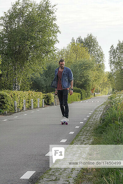 A man face the camera while riding a skateboard on an empty road