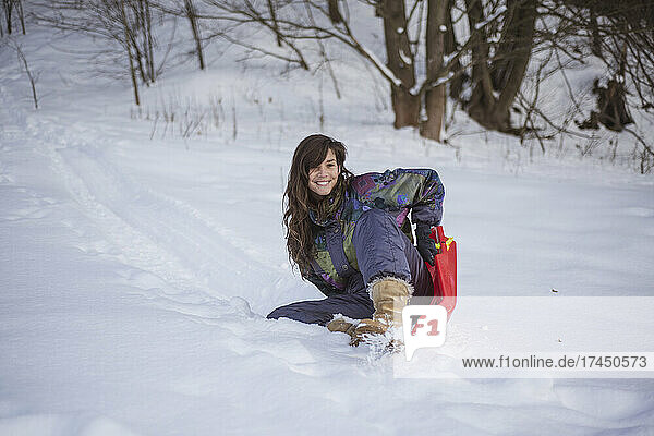 happy woman in snow suit smiles riding down hill on toboggan
