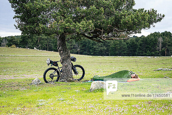 Woman sleeping in sleeping bag next to bicycle