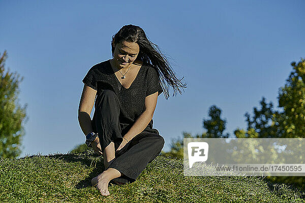 The girl in the black dress sitting in a green meadow with a blue sky