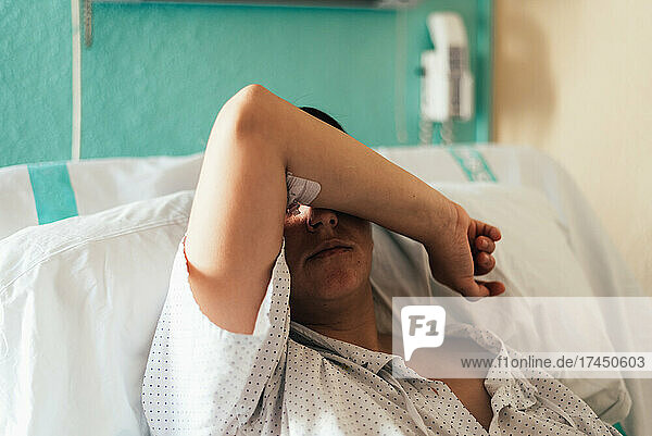 Young woman hospitalized in a bed. Gesture of pain and concern.