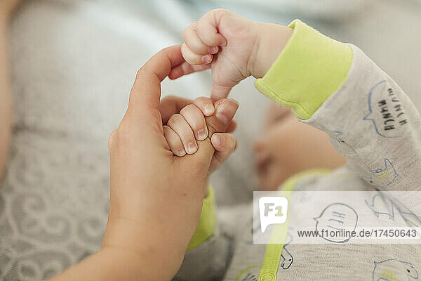 Infant baby holding mother's hand and finger while lying on bed