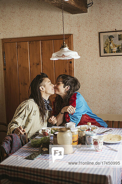 Queer female couple smile and kiss over birthday breakfast in Czechnia