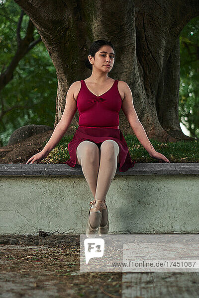 Hispanic young woman practices ballet with pointe shoes in a park.