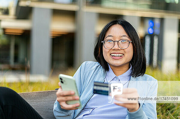 Young woman looking at camera holding credit card and cell phone
