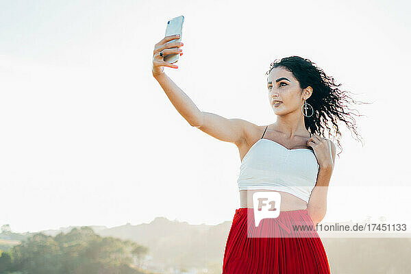 Young woman taking a selfie with her cell phone wearing a white top