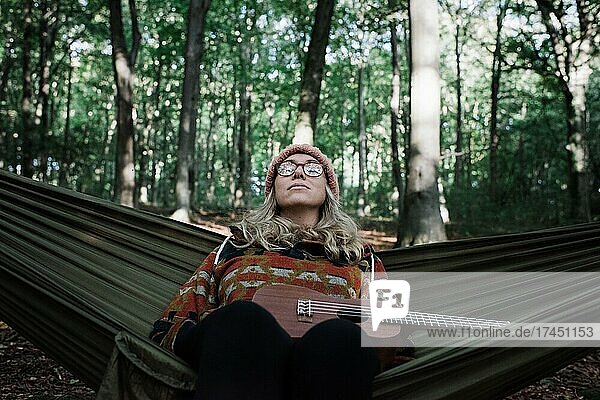 woman sat on a hammock enjoying the peace in a forest with a ukulele
