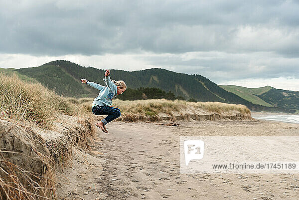 Preteen jumping on beach in New Zealand with mountains in background
