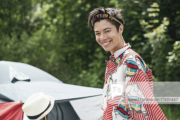 Smiling queer mixed-race woman colourful shirt  headpiece in campsite