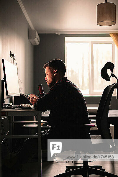 Man using smart phone and computer sitting at desk working at home