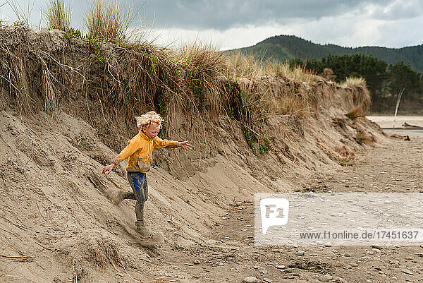 Blonde haired child running down sand dune in New Zealand
