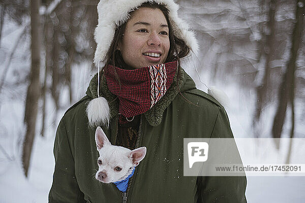 Androgynous asian woman with cute chihuahua inside her jacket in snow