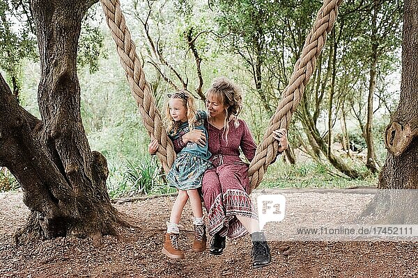 mother and daughter sat on an outdoor swing together hugging