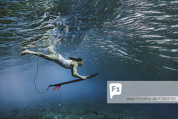 Male surfer holding surfboard while diving undersea at Maldives