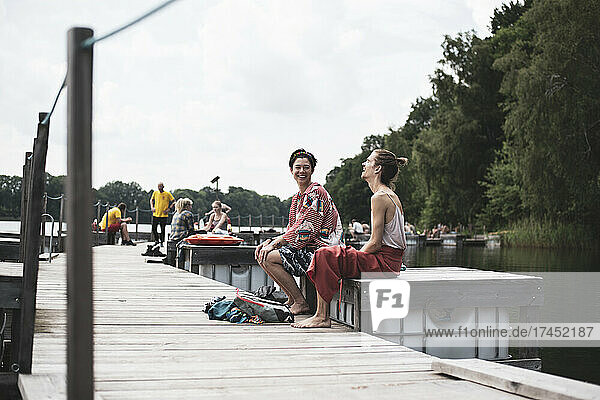 Mixed race friends laughing sitting on pier by lake in Poland