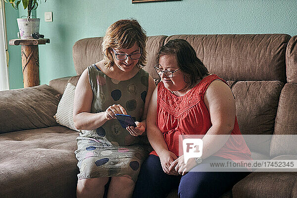 Adult woman and her sister with down syndrome look at a phone at home