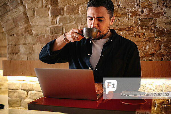 Businessman drinking coffee while using laptop computer at cafe