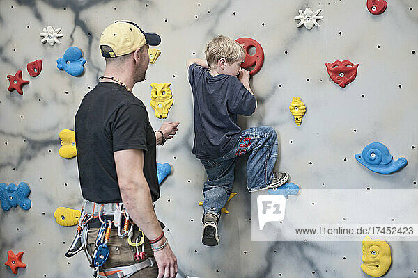climbing coach assisting young boy on bouldering wall