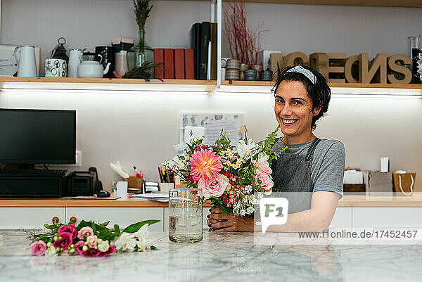 Smiling female florist holding a bouquet in her flower shop