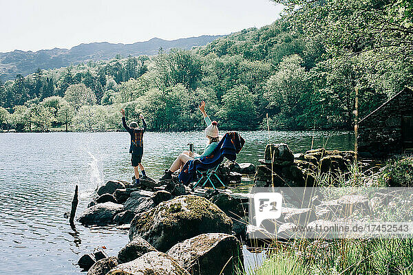 woman sitting on rocking chair by a lake whilst her kids throw rocks