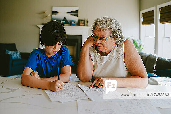 Grandmother helping grandson with writing homework at home.