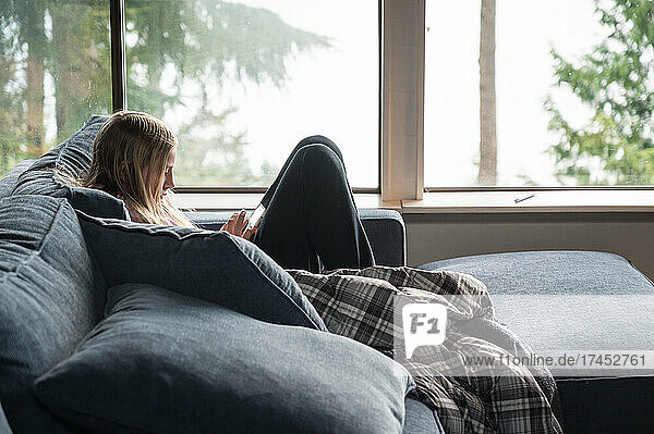 Young Teen Girl Lounging on Blue Sofa Looking at Phone