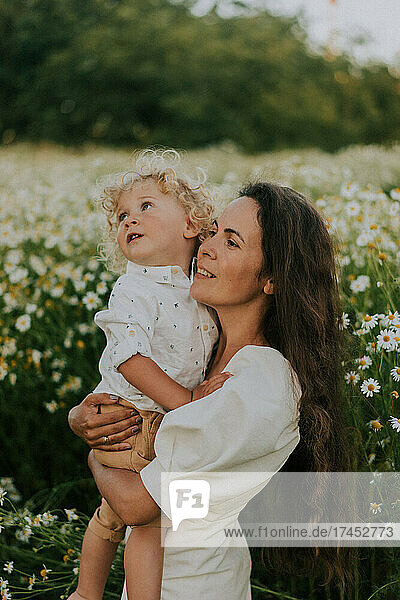A mother holds her son against the background of a chamomile field.