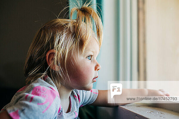 Blue eyed toddler girl looks out front window of Phoenix house