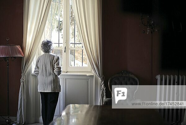 elderly lady looks out of a house window