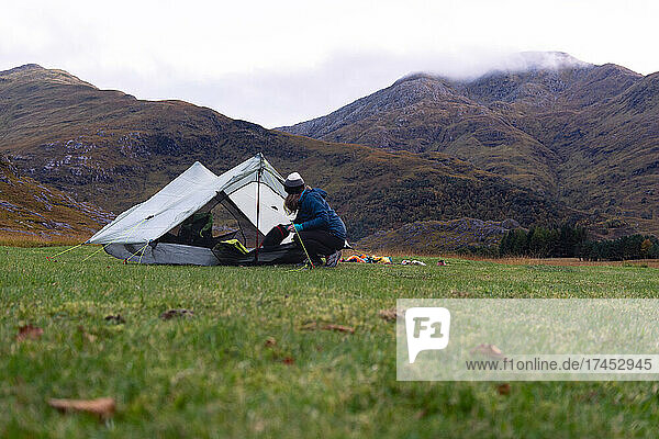 Female Camper setting up tent at foot of mountain