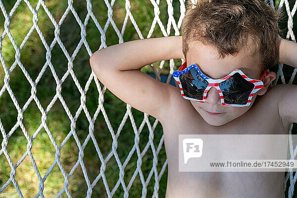 Close up of a young boy relaxing in hammock wearing silly sunglasses