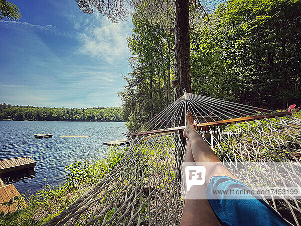 Female legs in the end of a hammock with a view of docks on a lake.