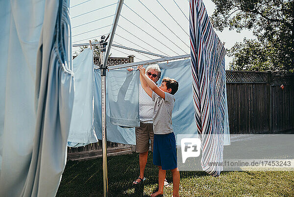 Older woman and boy hanging laundry on an outdoor clothesline.