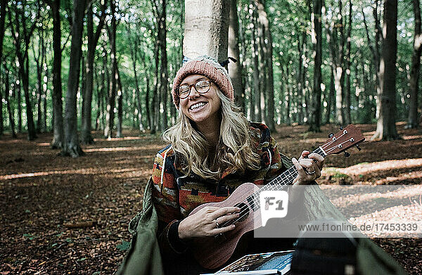 woman happily playing the ukulele in the forest on a hammock