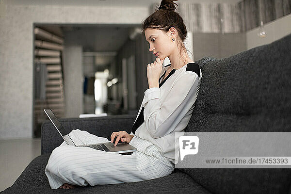 Thoughtful woman using laptop on sofa
