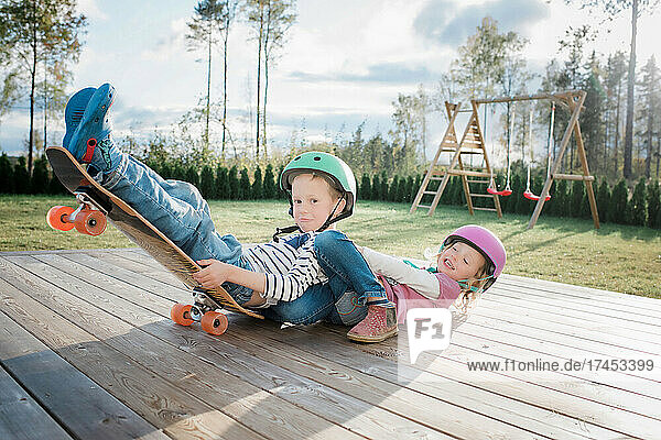 brother and sister playing on a skateboard at home together laughing