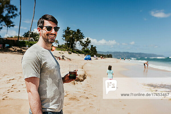 Man smiles at camera while drinking coffee on an Oahu beach
